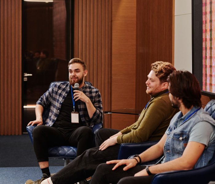pexels-photo-8348623-8348623 Men engage in a relaxed conversation during an indoor panel discussion.